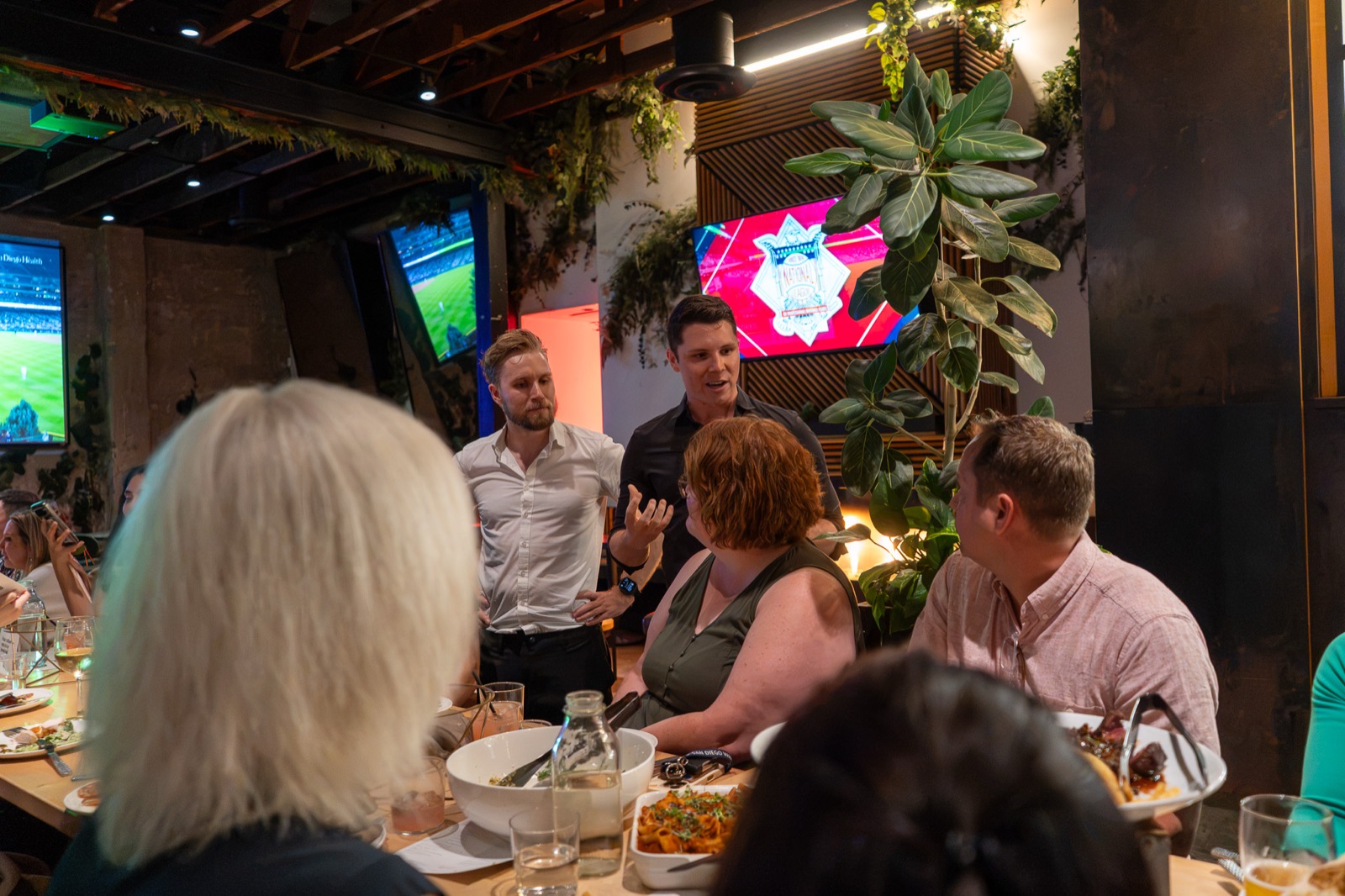 Guests in conversation across the table under the greenery of Nolita Hall